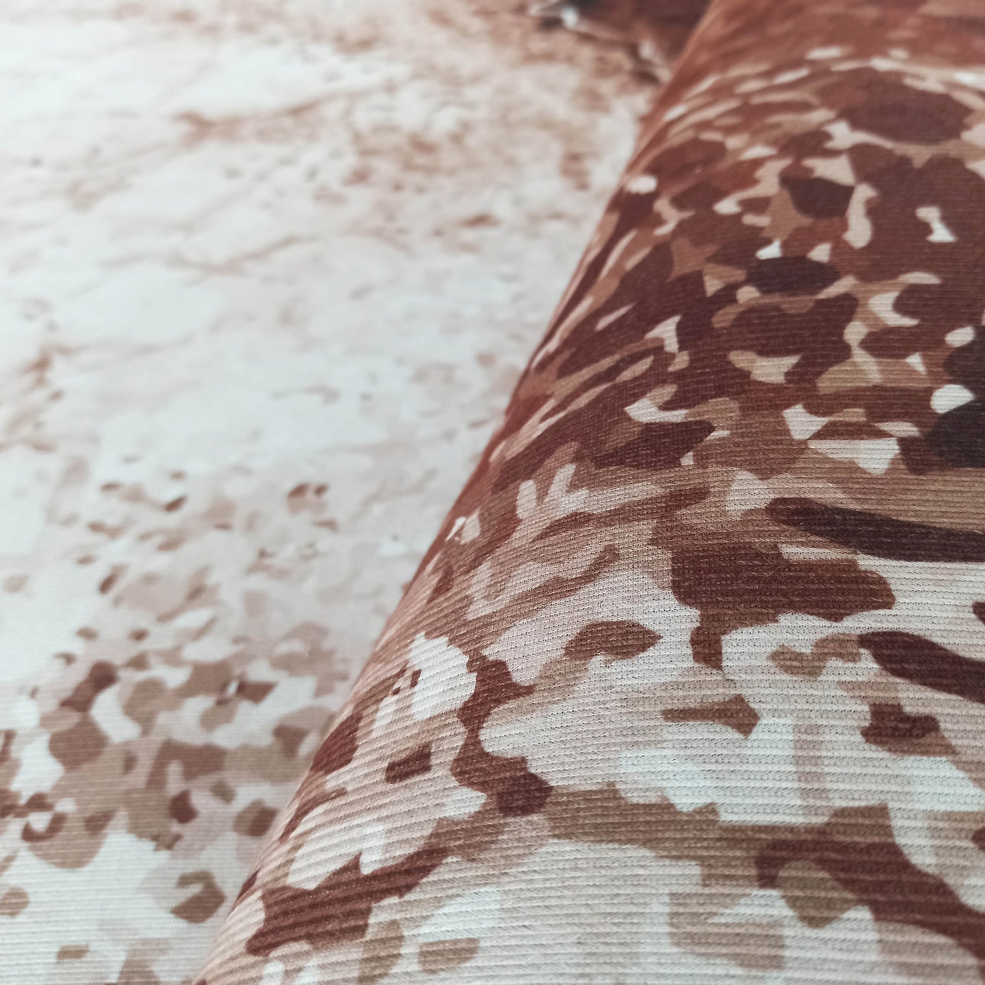 Gros plan sur un tapis texturé aux motifs abstraits et irréguliers dans des tons de marron, beige et crème, partiellement roulé