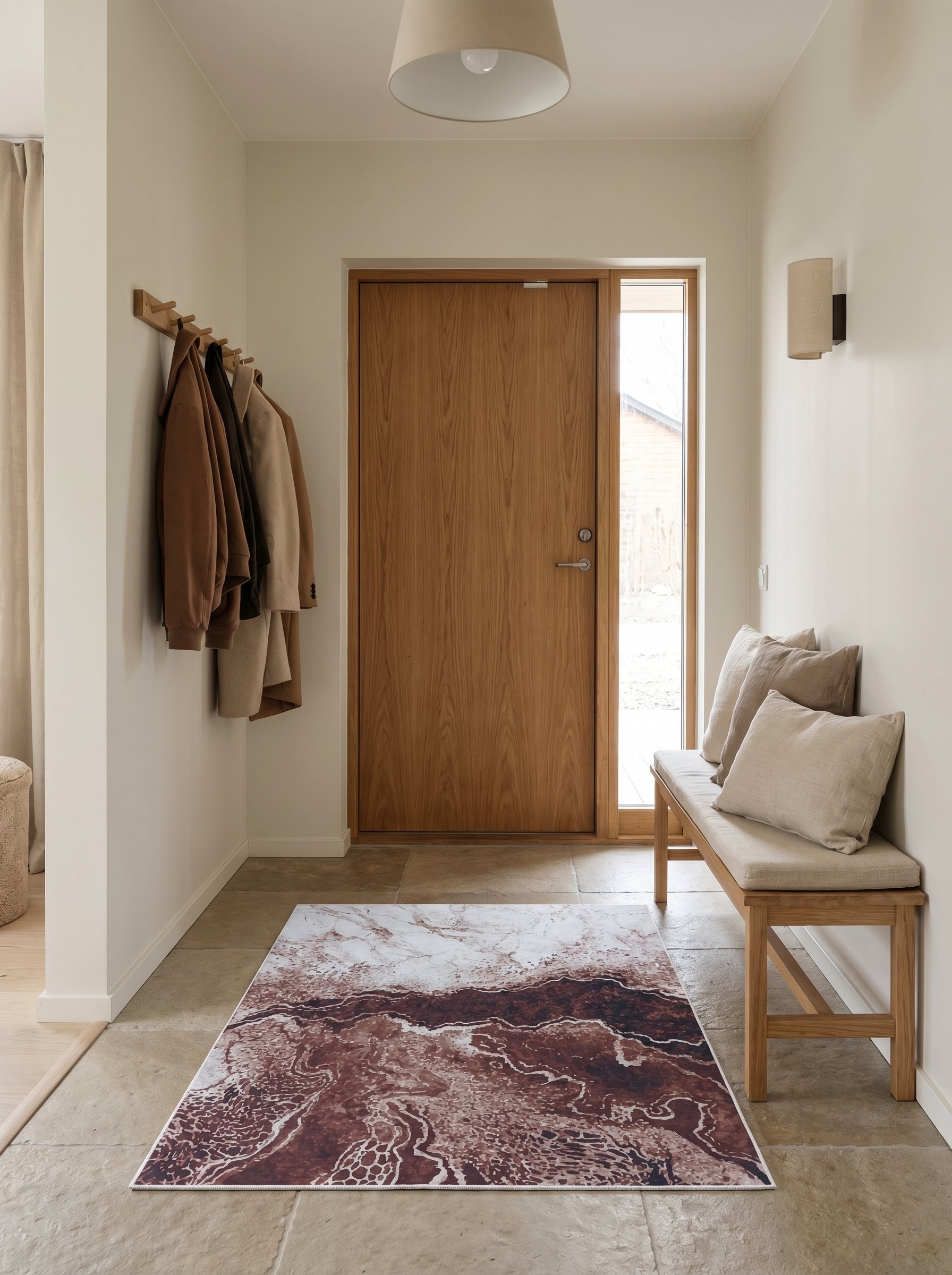 Tapis rectangulaire aux motifs organiques brun-rouge et crème rappelant des strates géologiques, étendu dans une entrée lumineuse