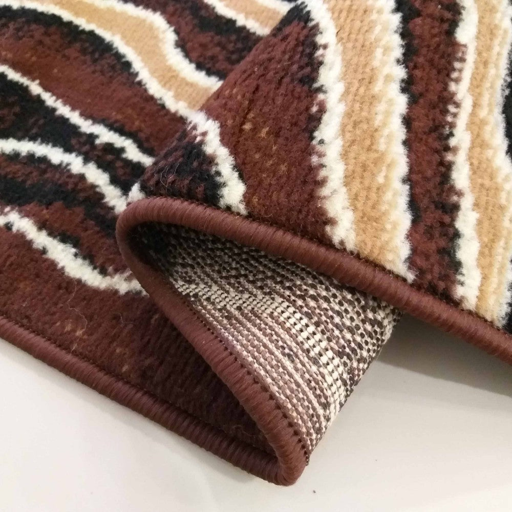 Tapis plié aux motifs ondulés marron, beige, noir et blanc, montrant sa texture douce et son envers tissé