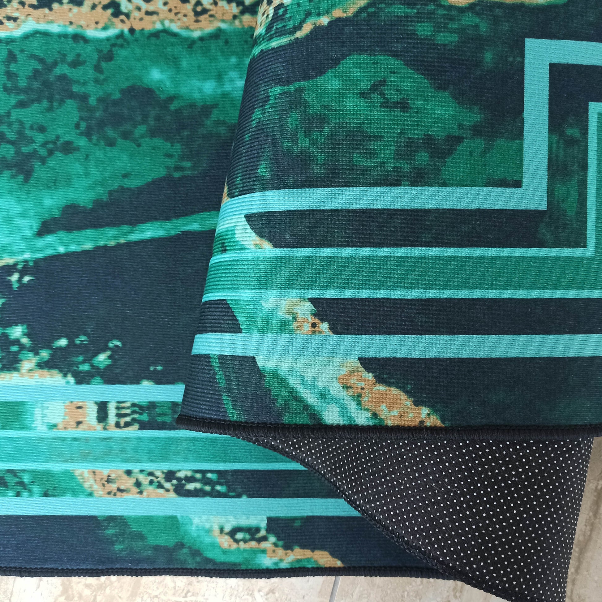 Tapis enroulé aux motifs abstraits vert émeraude, bleu foncé et beige, avec des bandes turquoise géométriques et un envers noir à pois