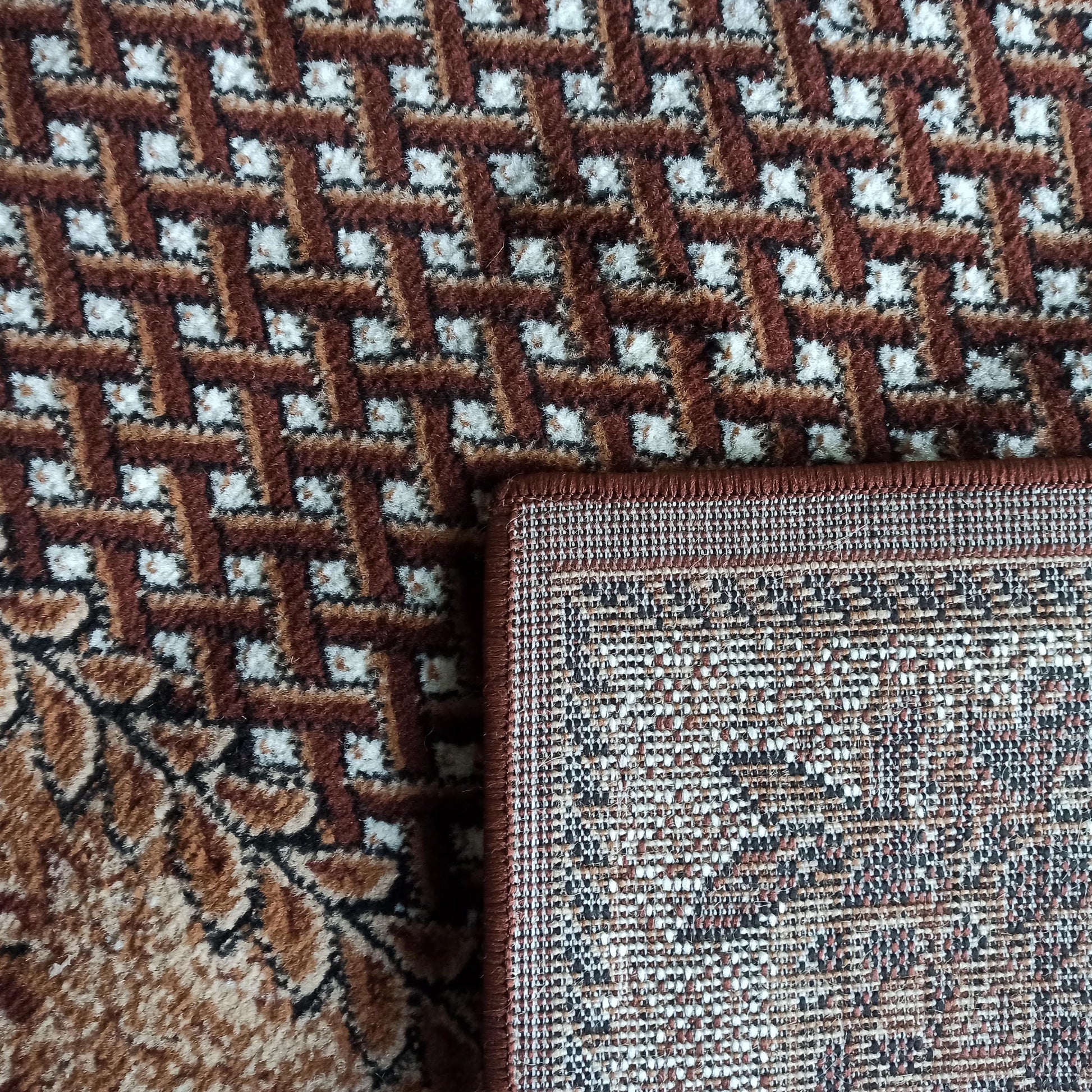 Gros plan sur un tapis moelleux à motif géométrique marron, blanc et noir, avec un coin révélant son envers tissé aux teintes variées