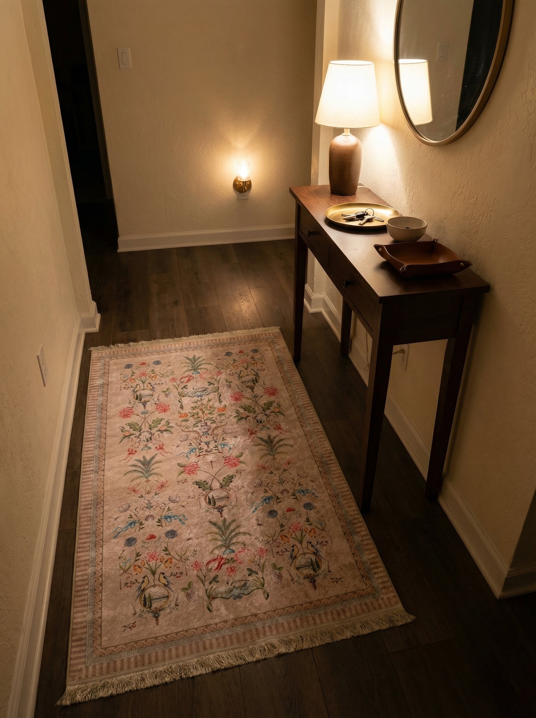 Tapis rectangulaire velouté beige rosé orné de motifs floraux, d'oiseaux et de rubans multicolores, avec franges, sur un parquet sombre dans une entrée chaleureuse