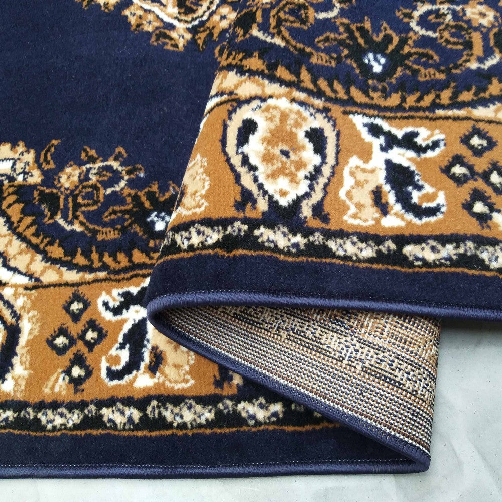 Tapis bleu marine à poils courts avec des motifs ornementaux classiques beiges, noirs et crème, un coin est replié