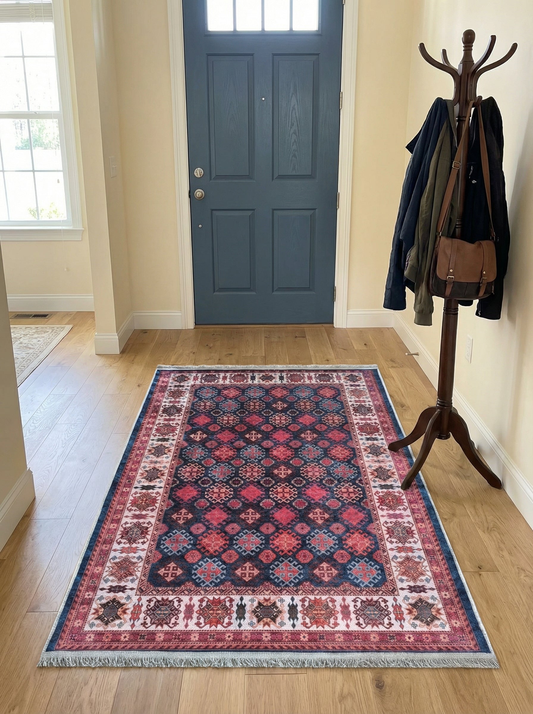 Tapis rectangulaire à motifs géométriques rouge foncé, bleu marine et rose clair, avec des franges, posé sur un plancher en bois dans une entrée
