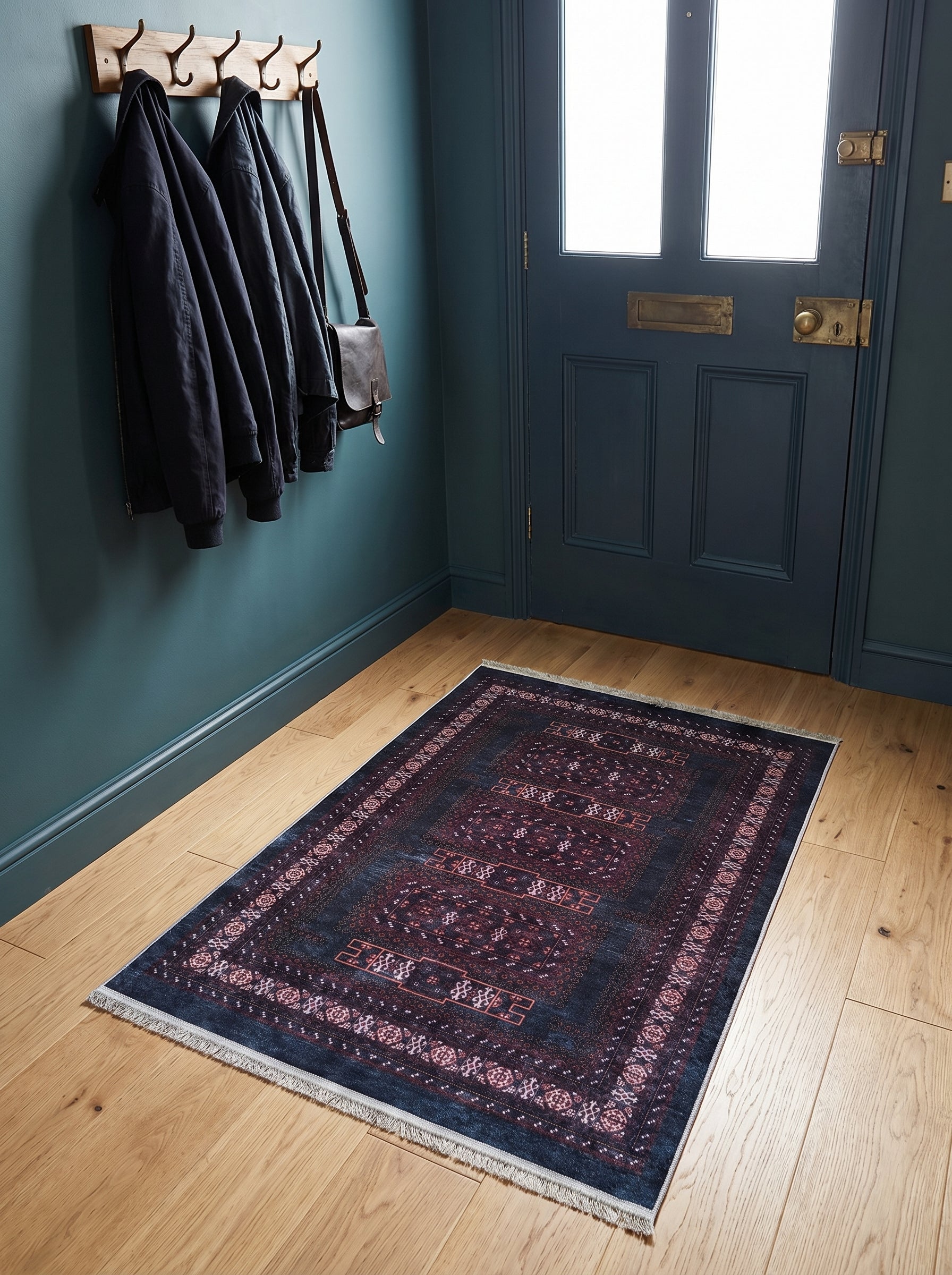 Tapis rectangulaire bleu marine avec motifs traditionnels rouges et bordeaux, à franges, posé sur un parquet clair dans une entrée aux murs bleu-canard