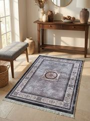 Tapis rectangulaire gris vieilli à motifs classiques crème et noirs, avec un médaillon central orné, posé sur un sol carrelé dans une pièce décorée