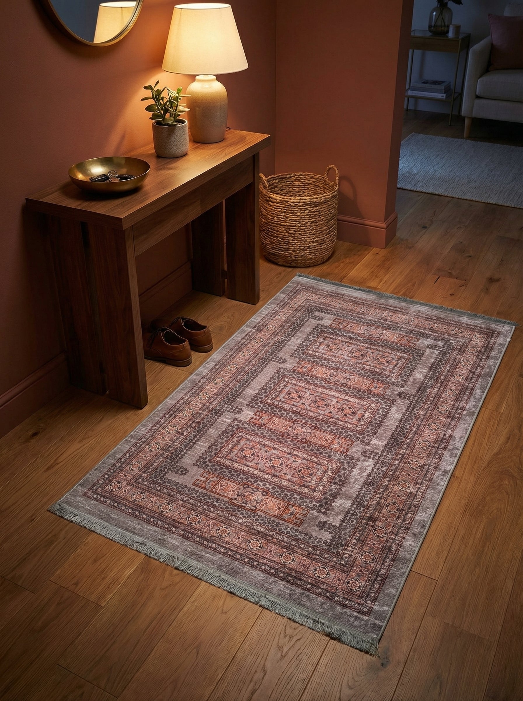 Tapis rectangulaire à motifs géométriques gris, rouille et noirs avec franges, posé sur un parquet dans une entrée