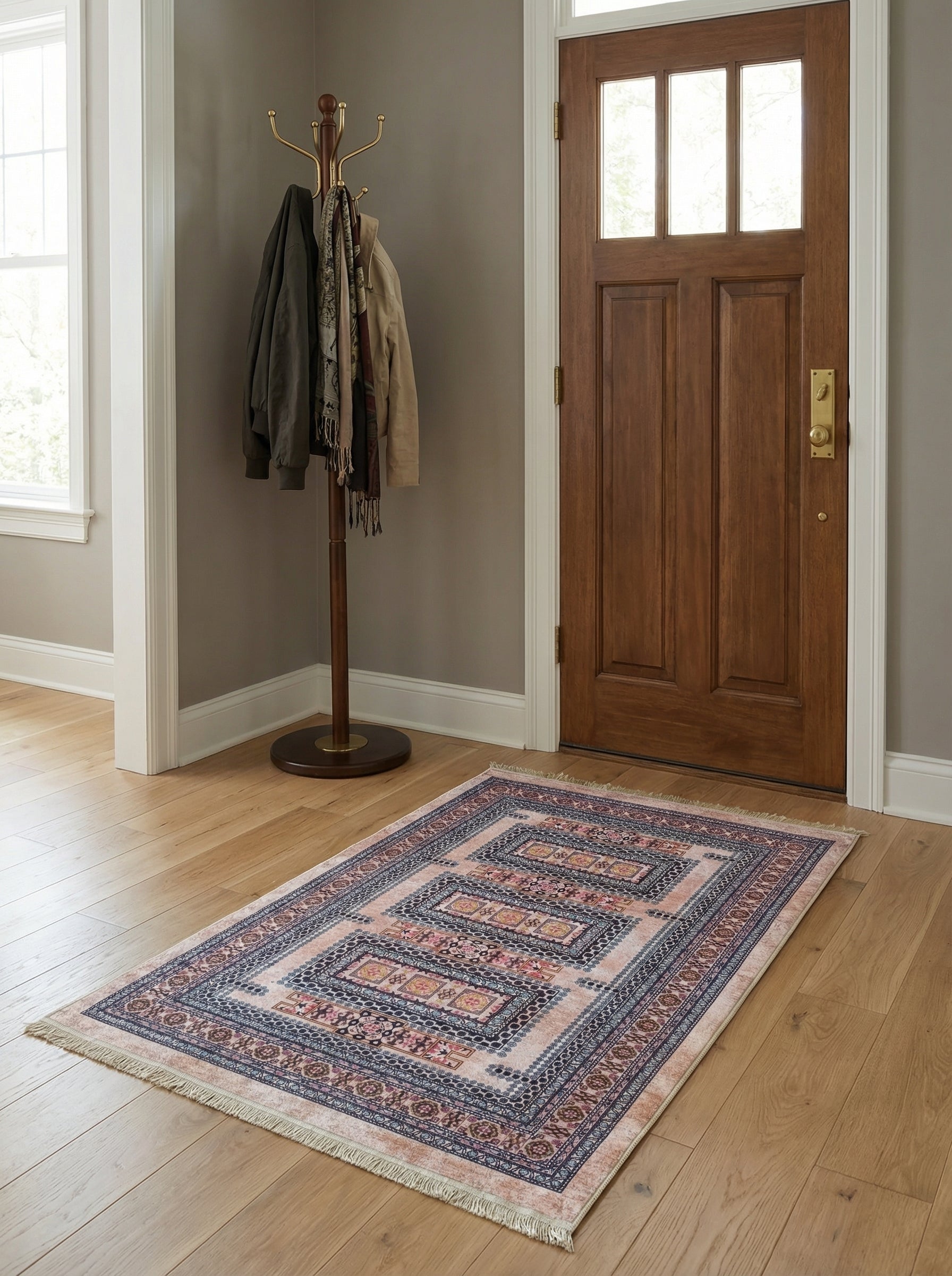 Tapis rectangulaire tissé, motifs géométriques et floraux rose pâle, bleu foncé et beige avec franges, sur parquet dans une entrée
