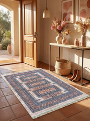 Tapis rectangulaire aux motifs géométriques traditionnels rose pâle, bleu marine et blanc, à franges, sur un sol carrelé d'une entrée