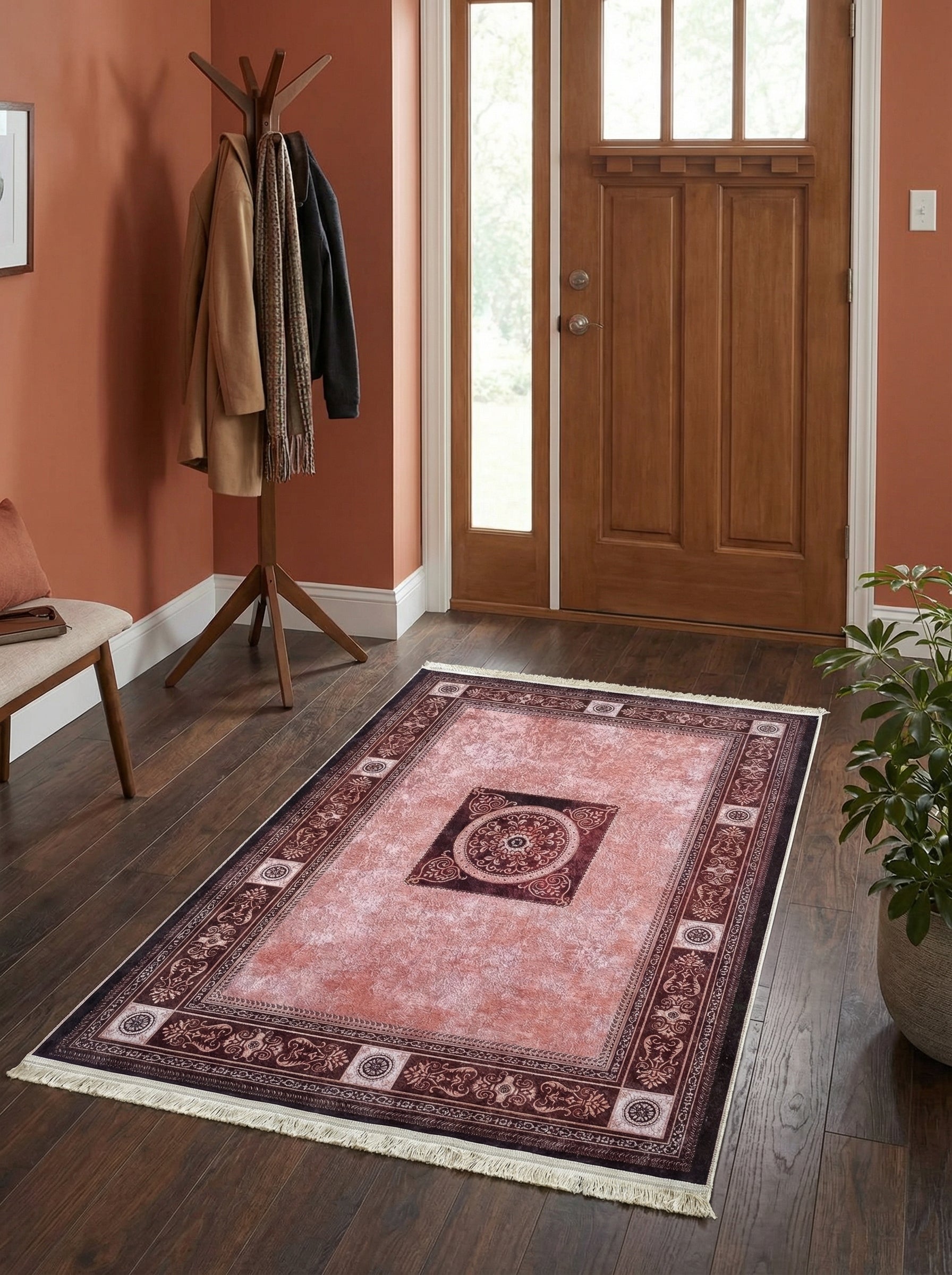 Tapis rectangulaire rose corail avec motifs bordeaux ornementaux et médaillon central, sur parquet en bois dans une entrée