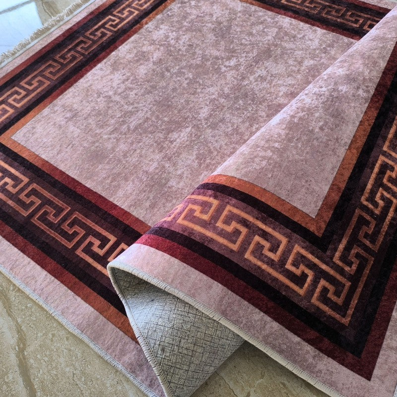 Tapis textile clair à l'aspect texturé, bordé d'un motif de clé grecque marron, rouge et orange, partiellement enroulé