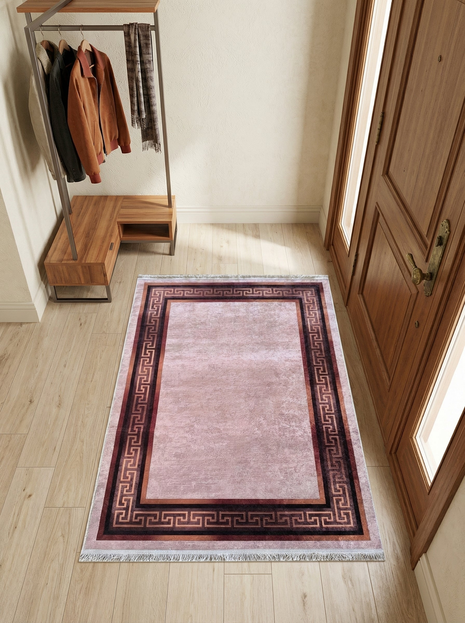 Tapis rectangulaire rose poudré texturé, bordé d'un motif géométrique grec marron foncé et terracotta, sur un parquet d'entrée