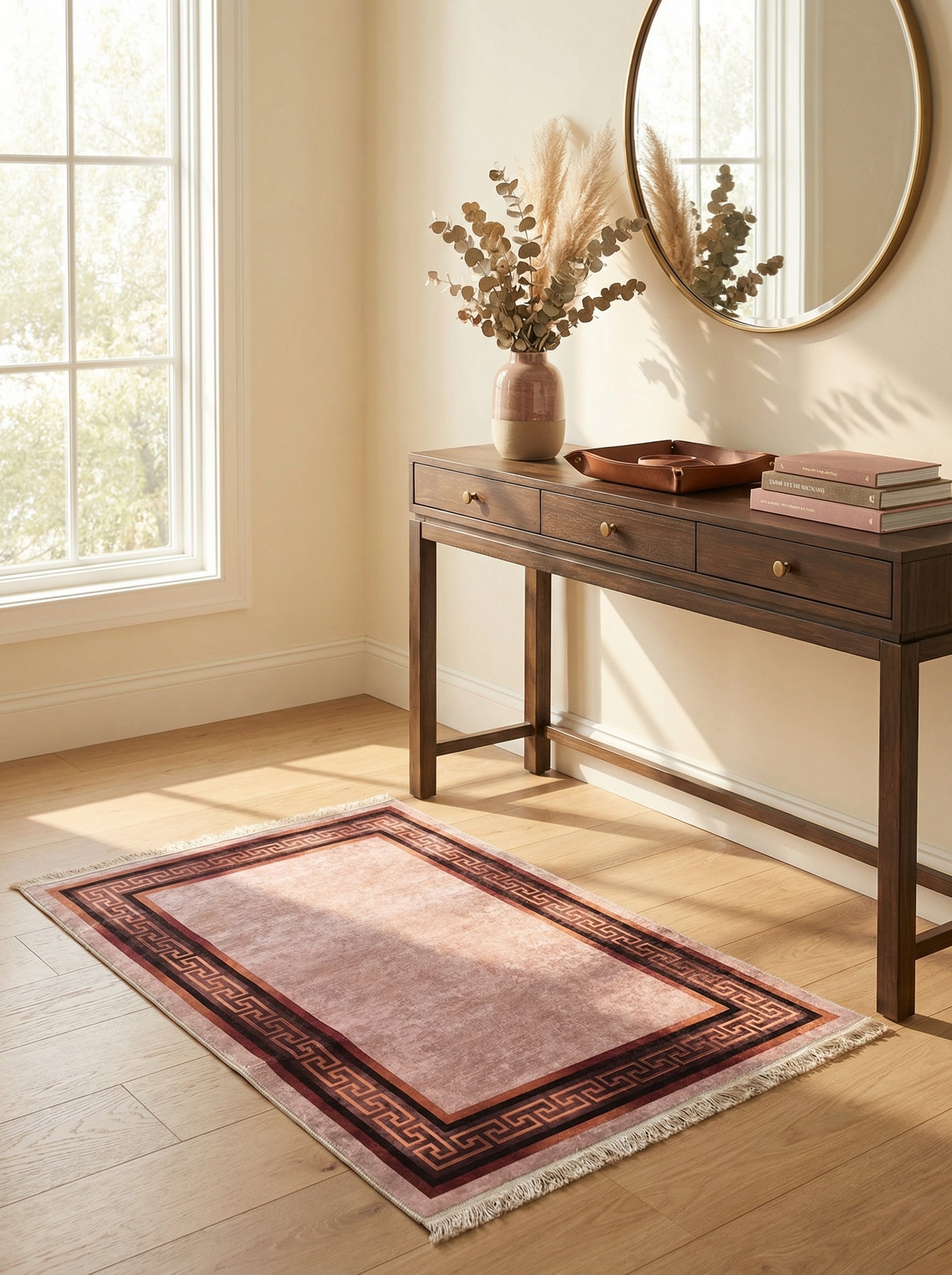 Tapis rectangulaire rose pâle à motifs méandre foncés, bordé de franges claires, posé sur un parquet en bois clair dans une entrée