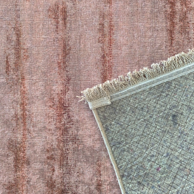 Tapis rose et bordeaux à l'aspect doux et motifs subtils. Un coin est relevé, révélant l'envers en tissu gris et les franges claires
