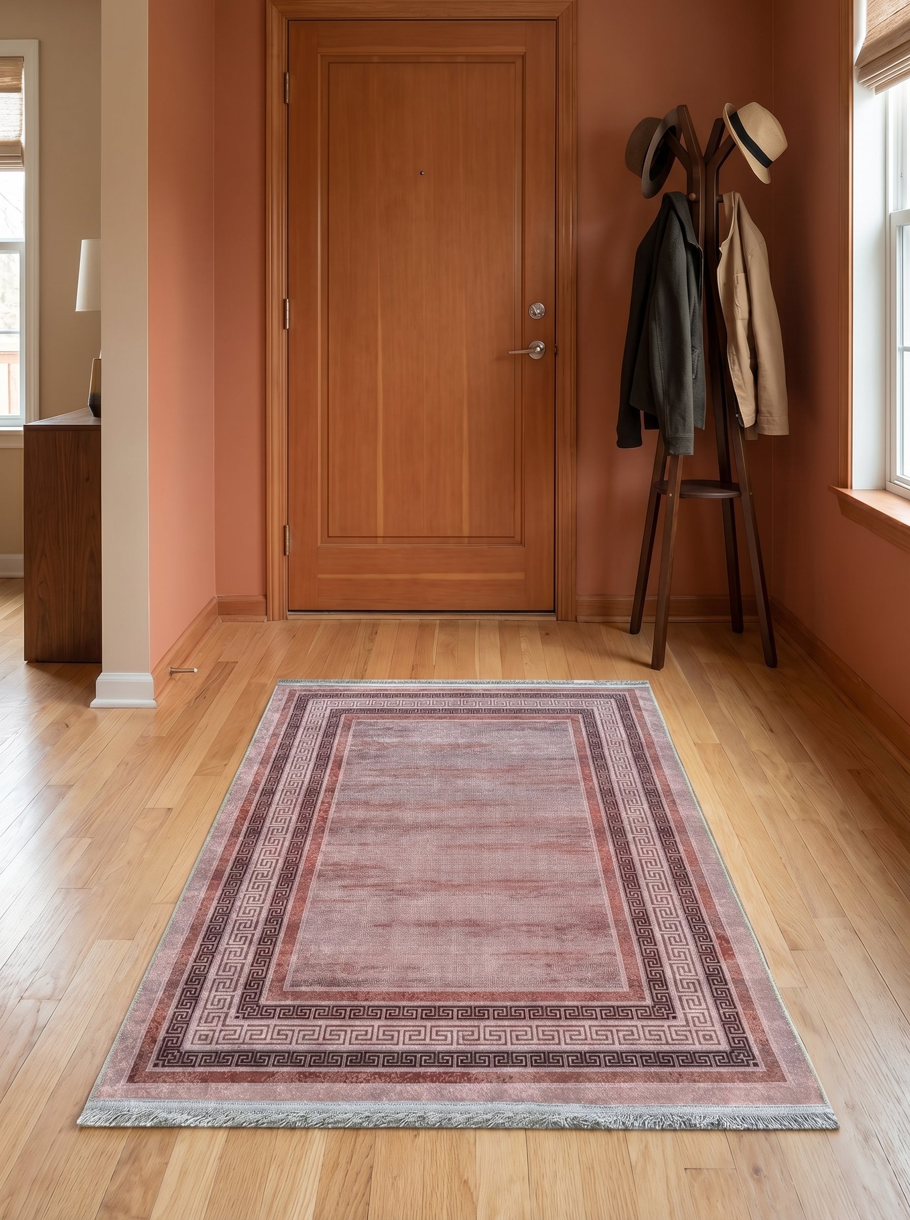 Tapis rectangulaire rose terracotta délavé à franges, avec bordure à motifs grecs marron foncé, sur parquet d'entrée