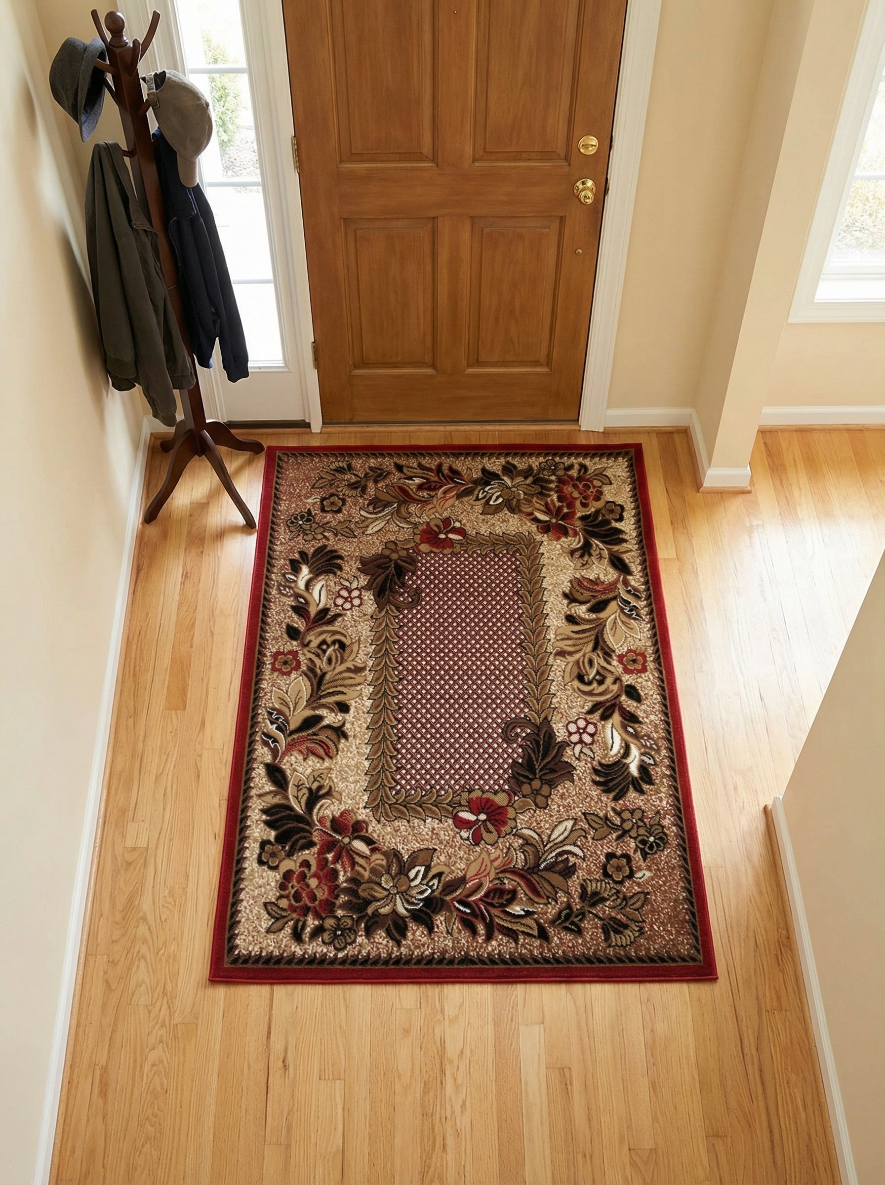 Tapis rectangulaire aux motifs floraux complexes rouge, marron et beige, avec un cadre rouge vif, au sol d'une entrée avec parquet clair