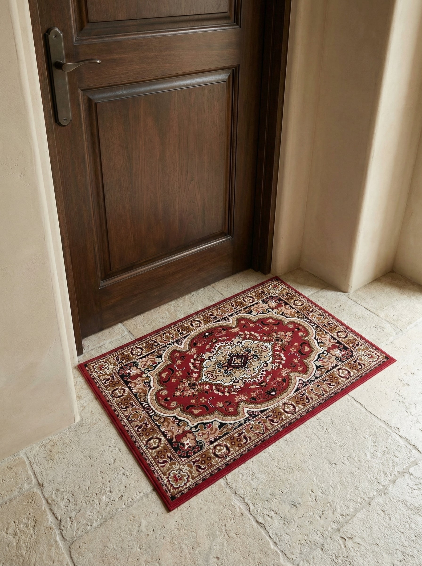 Tapis d'entrée rectangulaire rouge à motifs orientaux beiges et marron, posé sur un sol en pierre claire devant une porte en bois sombre