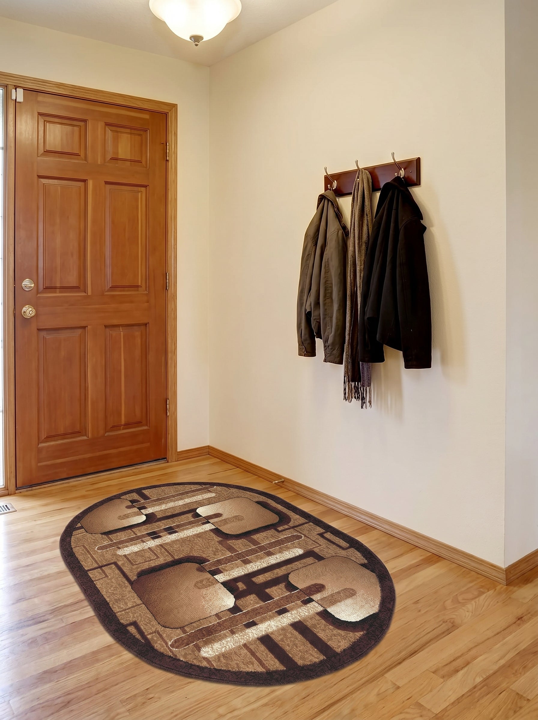 Tapis ovale aux motifs géométriques marron, beige et crème avec un liseré foncé, sur un parquet clair d'entrée