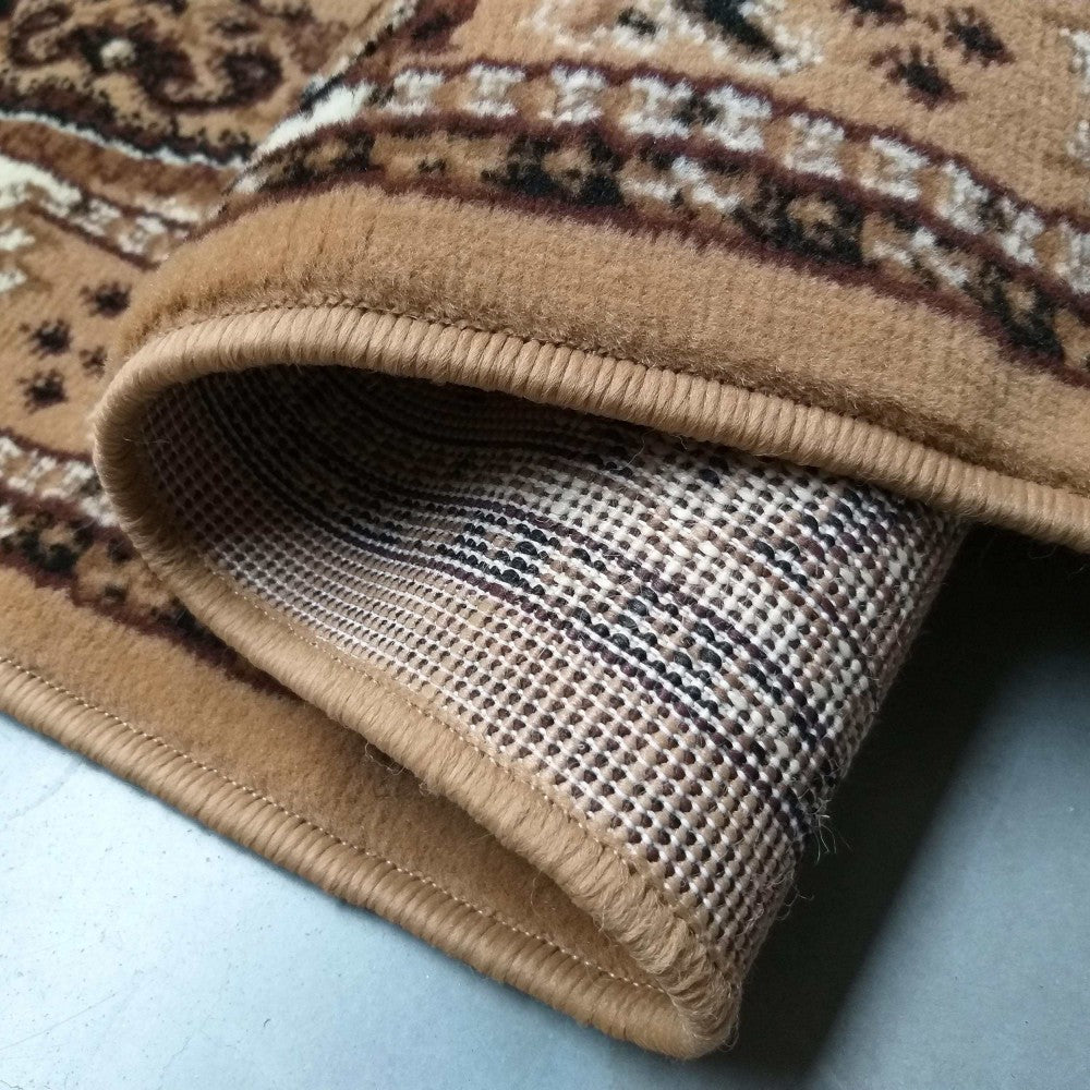 Tapis beige plié avec un motif ornemental marron foncé et crème, montrant son envers texturé en grille