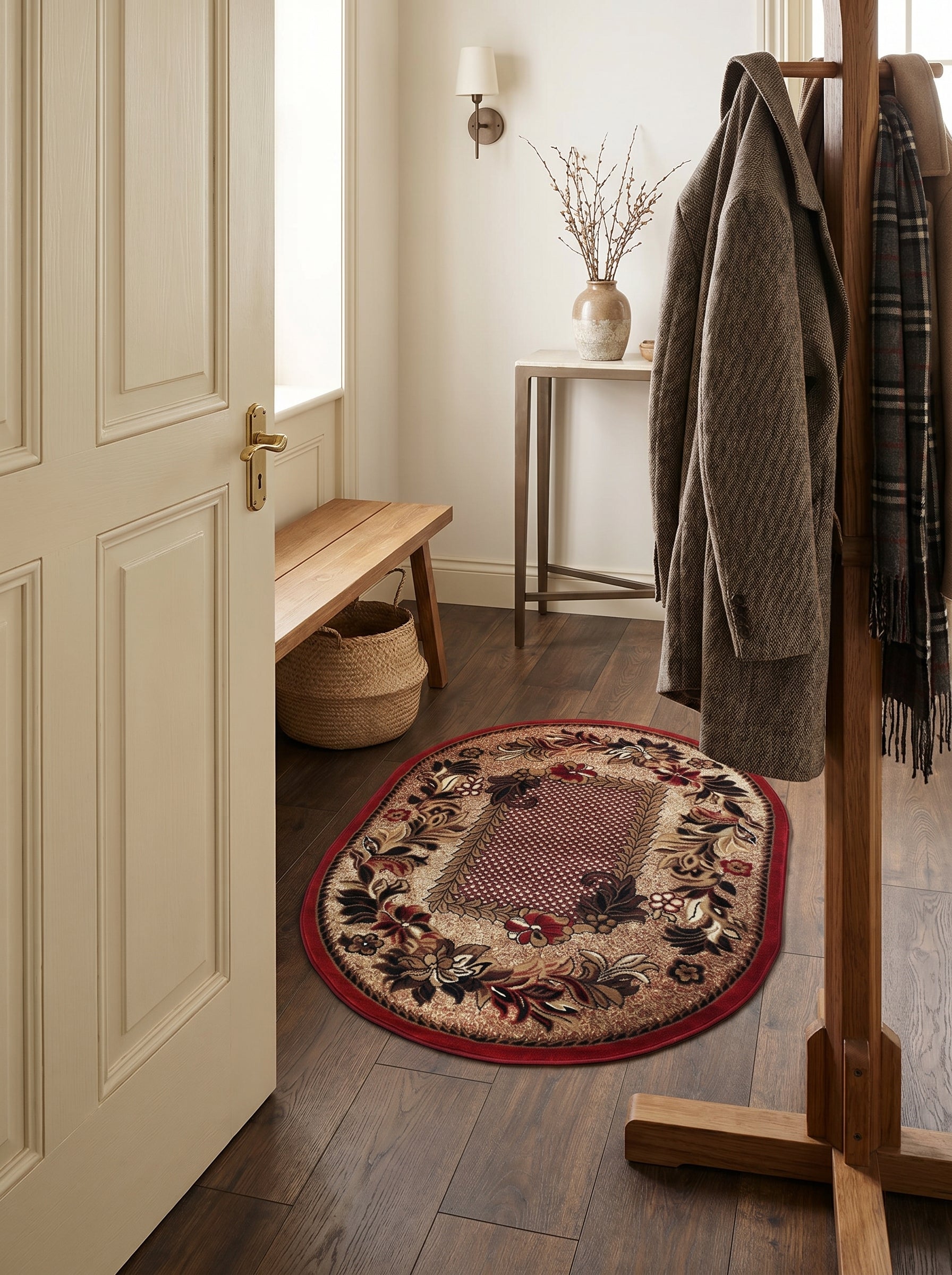 Tapis ovale traditionnel aux motifs floraux marron, beige et rouge bordeaux, avec un encadrement rouge, posé sur un parquet d'entrée