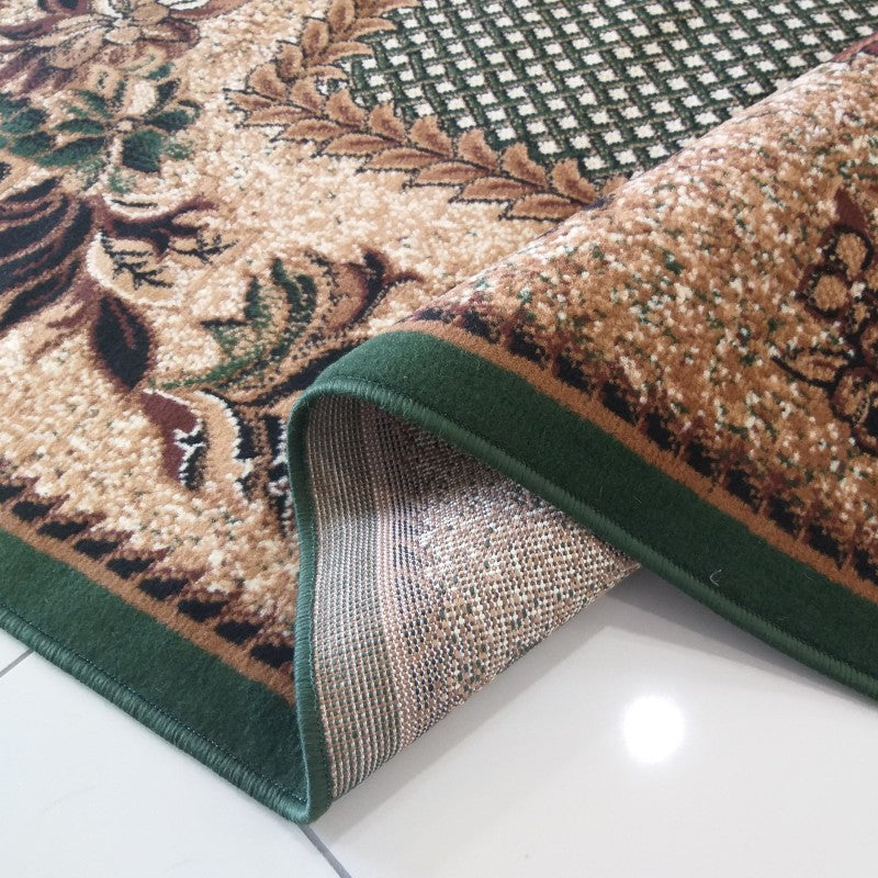 Tapis beige à motifs floraux et géométriques marron et verts, bordure vert foncé, l'envers du tapis est visible
