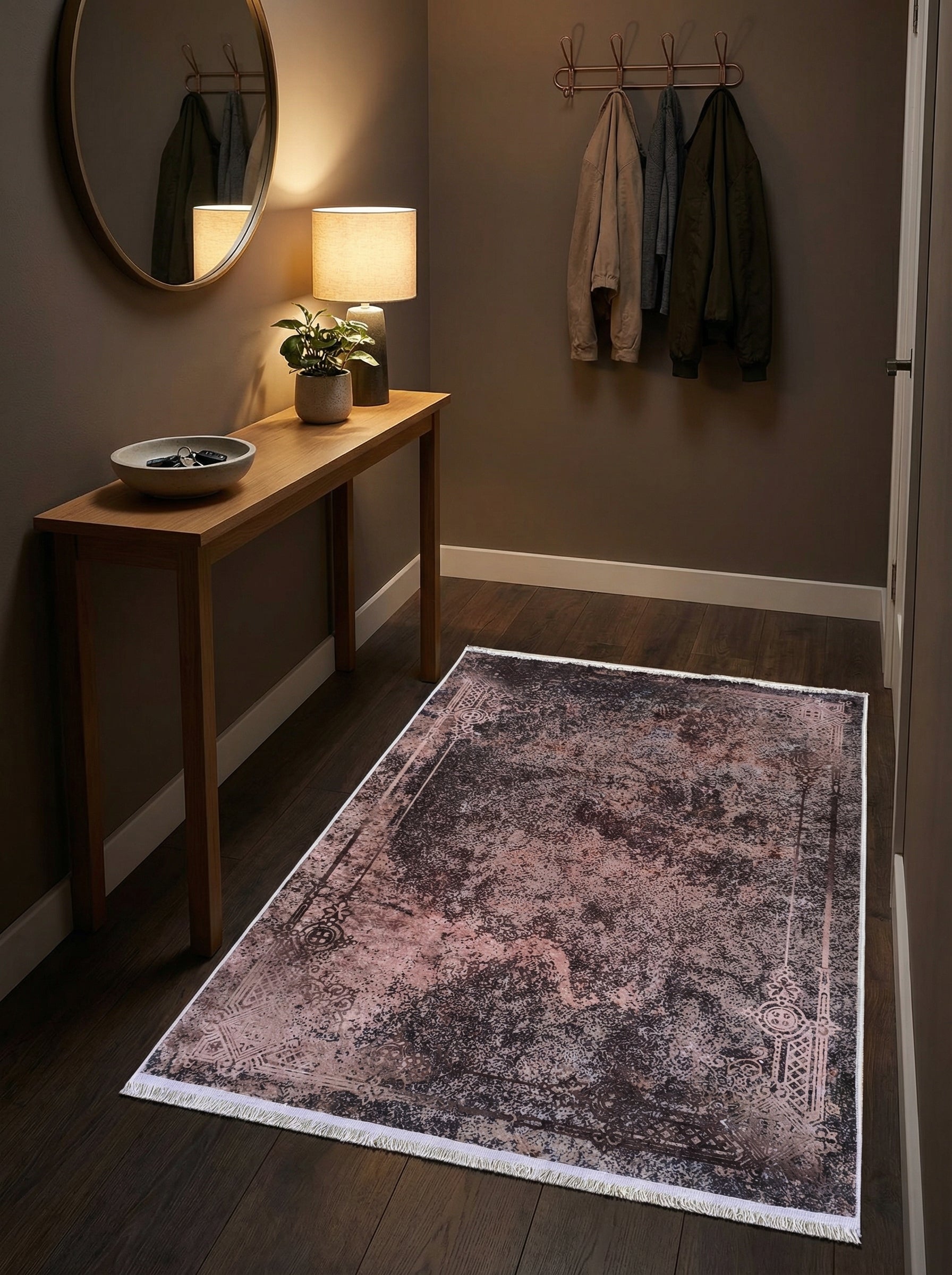 Tapis rectangulaire avec un motif abstrait et délavé rose poudré, marron foncé et blanc, frangé, sur un parquet sombre dans une entrée