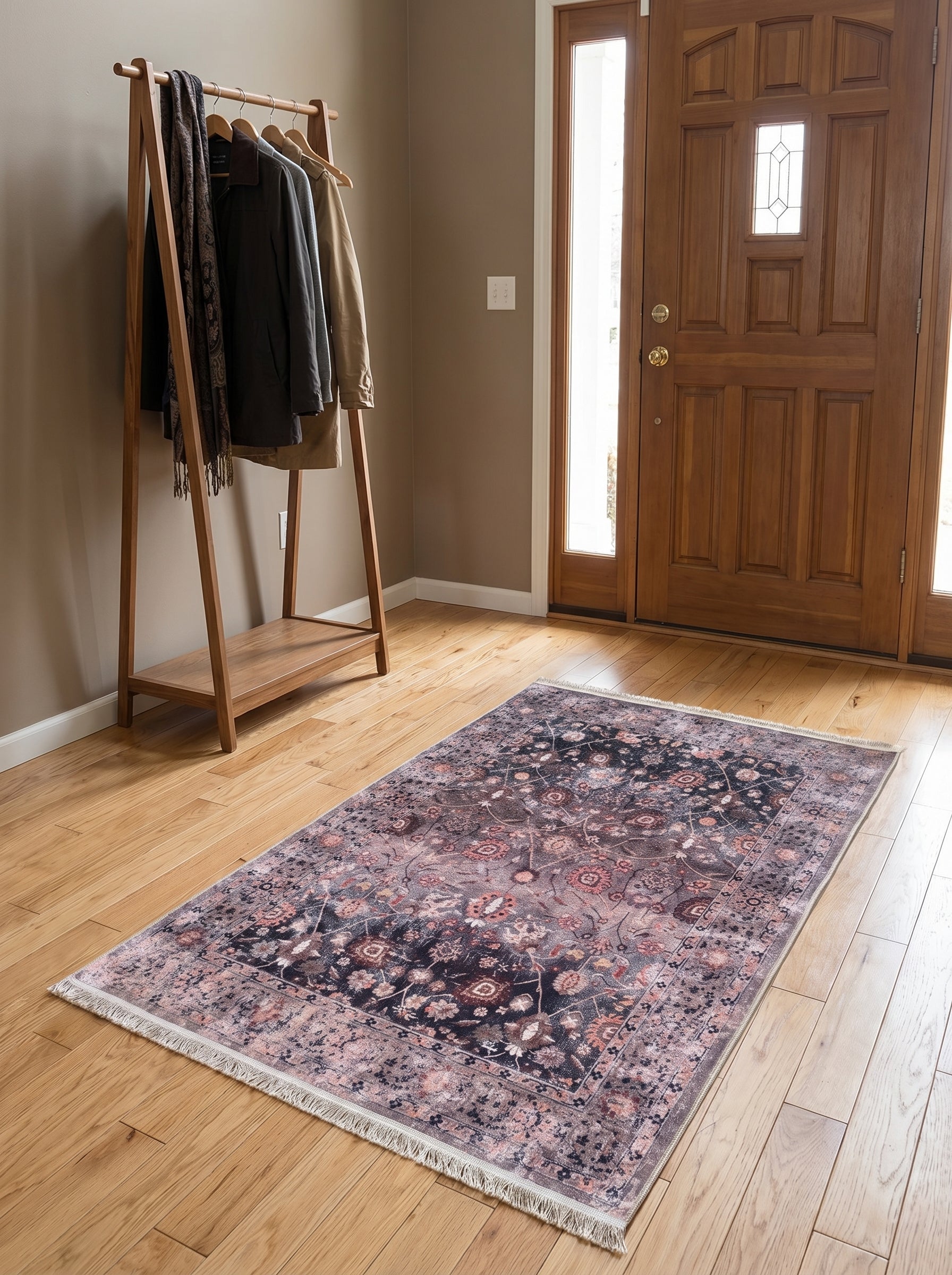 Grand tapis rectangulaire aux motifs floraux délavés en bleu foncé, rose et rouille, avec bordure assortie et franges, posé sur un parquet clair dans une entrée