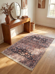 Tapis rectangulaire vieilli, motifs floraux traditionnels en noir, rose poudré et rouille, avec franges, sur parquet clair dans une entrée