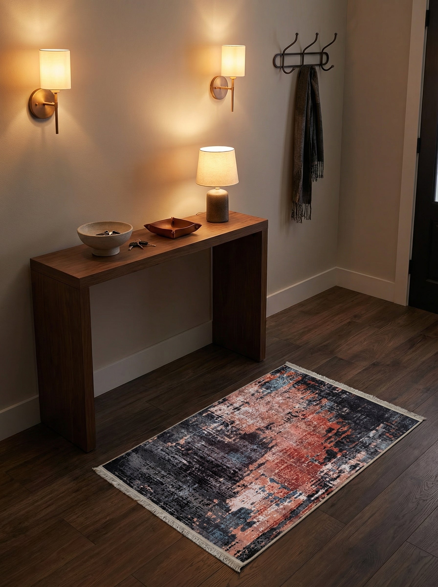 Tapis rectangulaire à motifs abstraits noirs, rouille et bleus avec franges, posé sur un parquet foncé dans une entrée