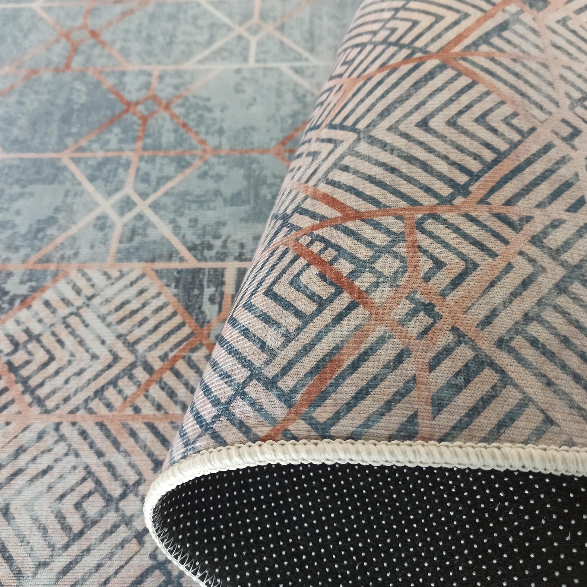 Tapis roulé avec motif géométrique bleu-gris et terracotta, montrant sa sous-face noire à pois et sa bordure blanche
