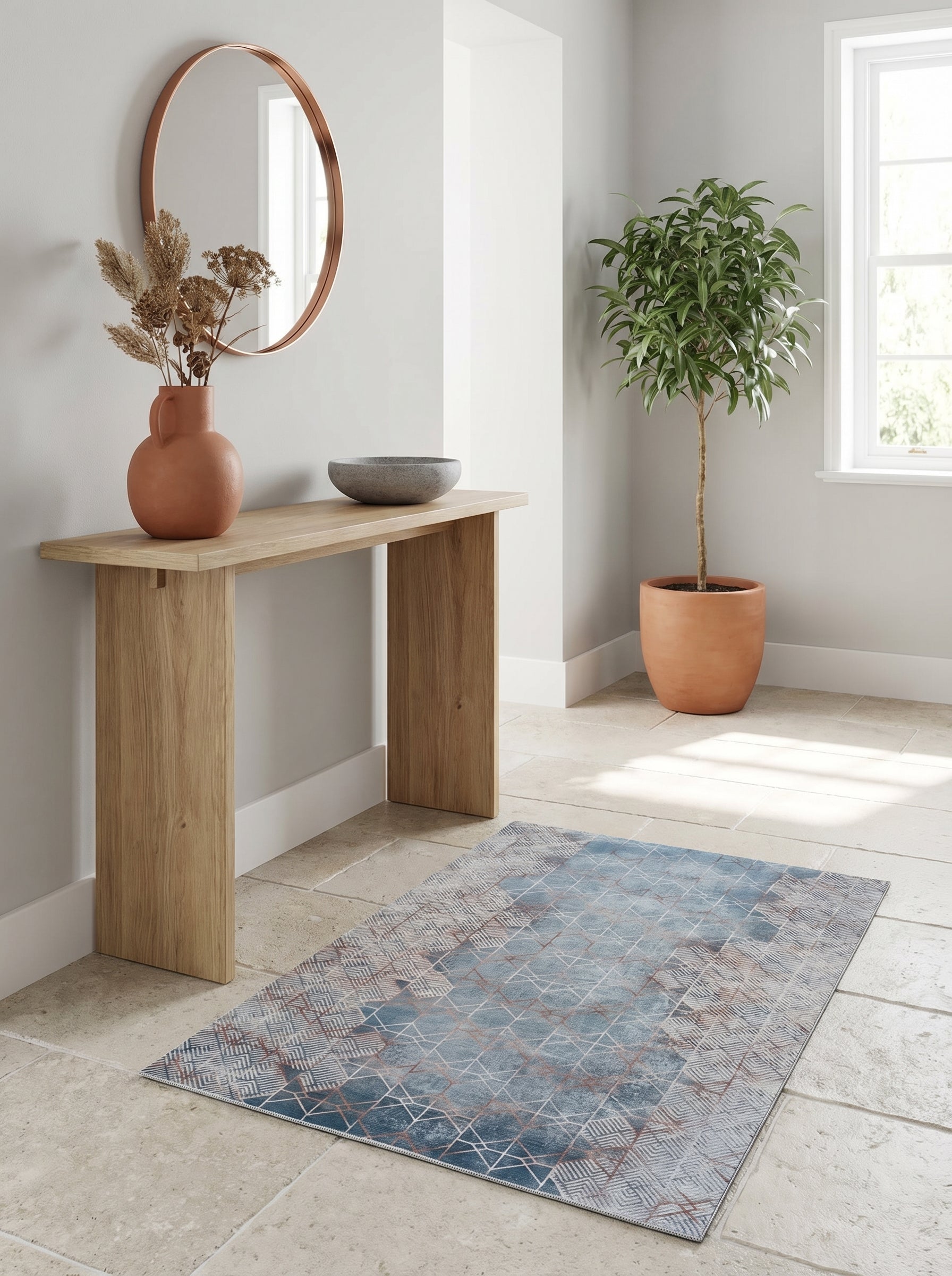 Tapis rectangulaire bleu délavé à motifs géométriques en losanges cuivrés et bandes grises, posé sur un sol en pierre dans une entrée lumineuse