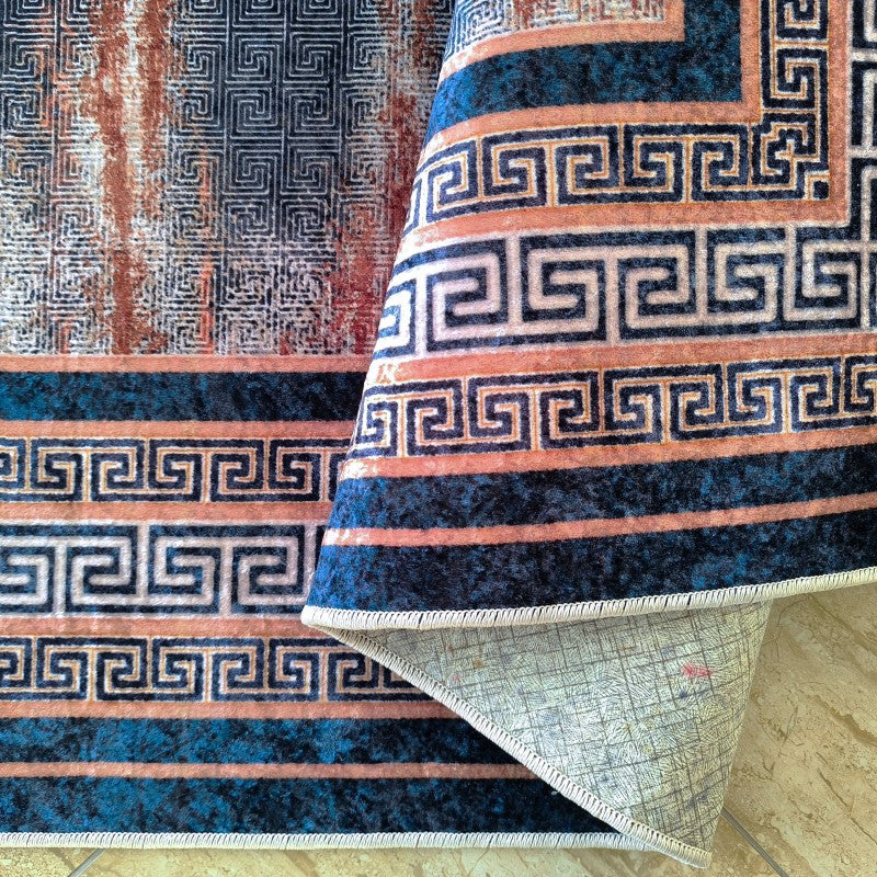 Tapis moelleux aux motifs géométriques méandres bleu marine et terracotta, montrant son envers clair et plié sur le carrelage