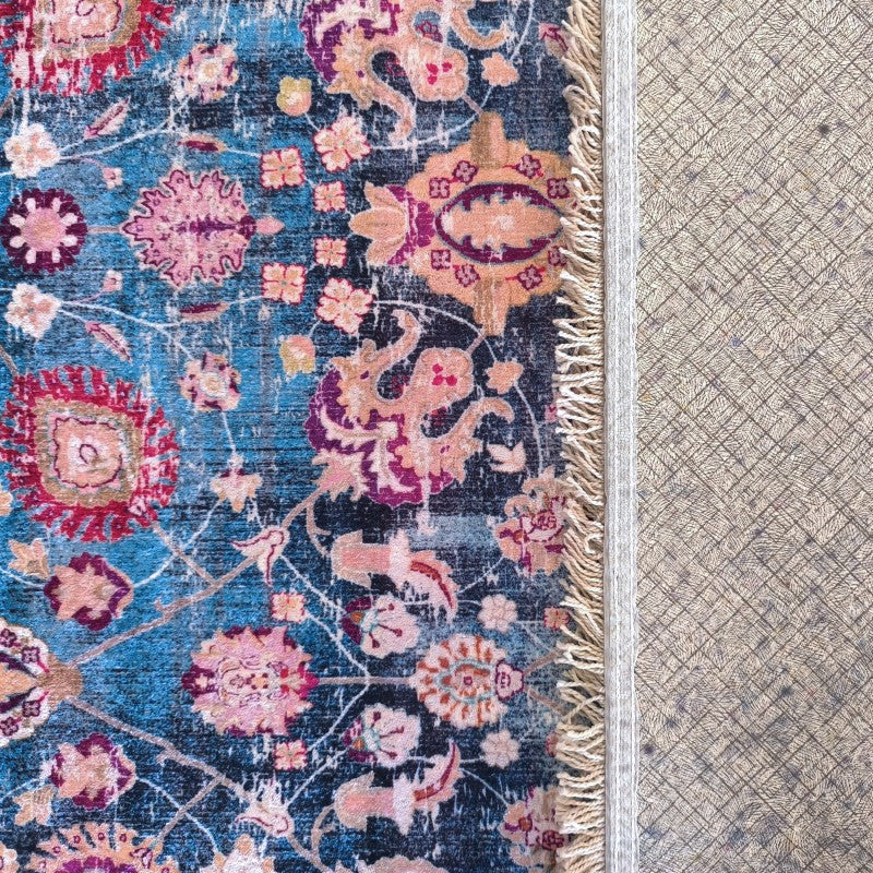Tapis coloré aux motifs floraux bleus, roses, fuchsia et pêche, avec des franges crème, et son envers texturé beige