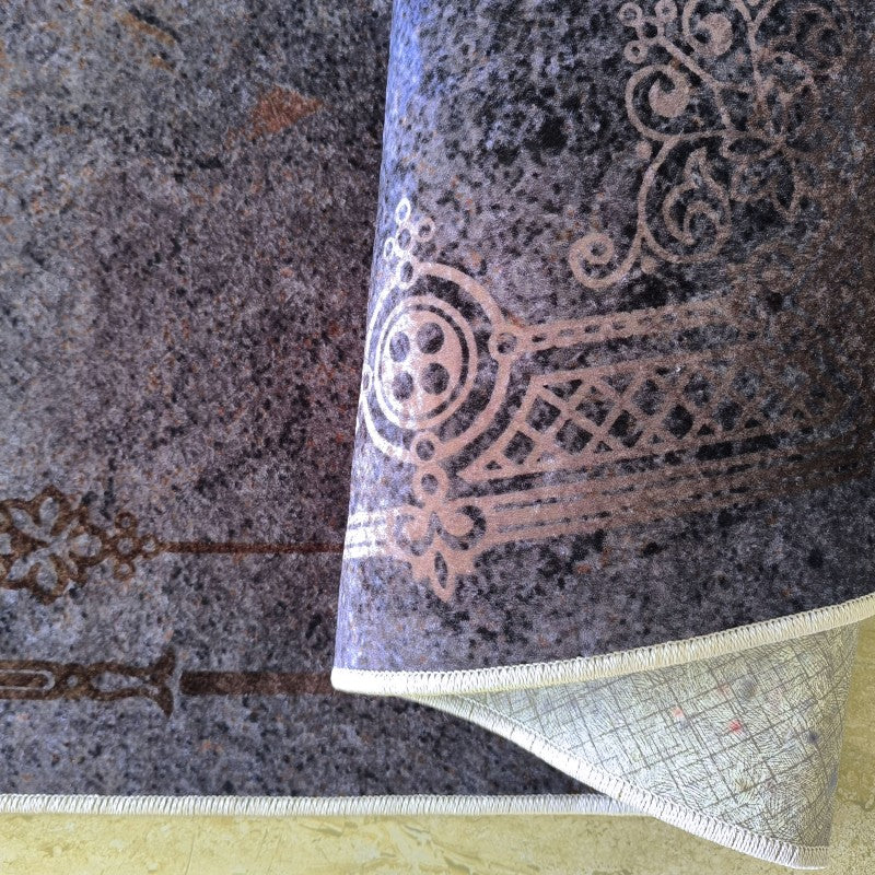 Tapis roulé à motifs ornementaux beige clair sur fond gris foncé avec des touches de brun, son dessous quadrillé et un bord surpiqué