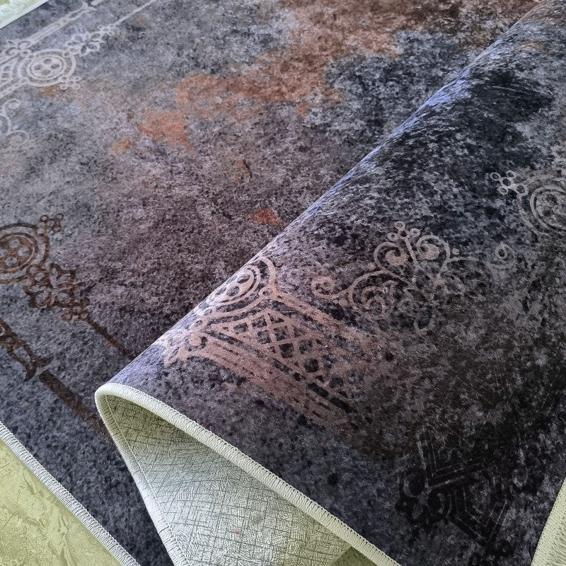Tapis à motifs ornementaux gris foncé et rouille sur fond texturé, partiellement roulé pour révéler son envers clair