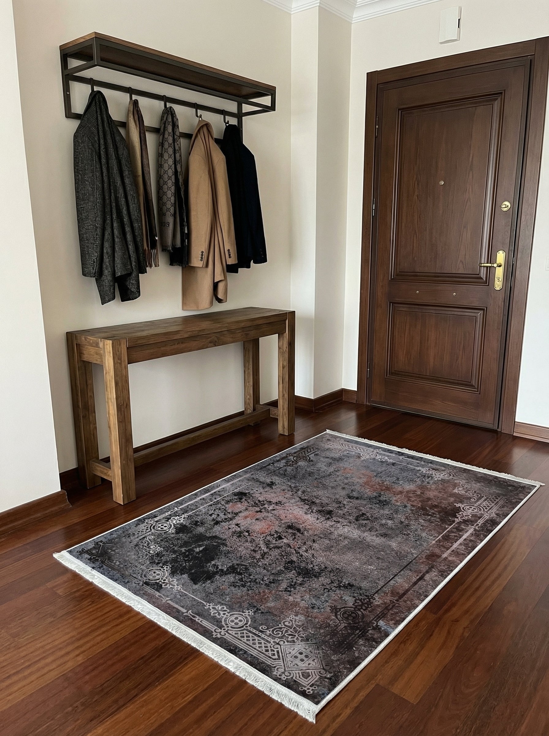 Tapis rectangulaire gris, noir et rouille aux motifs abstraits et bordure ornementée blanche, posé sur le parquet d'une entrée