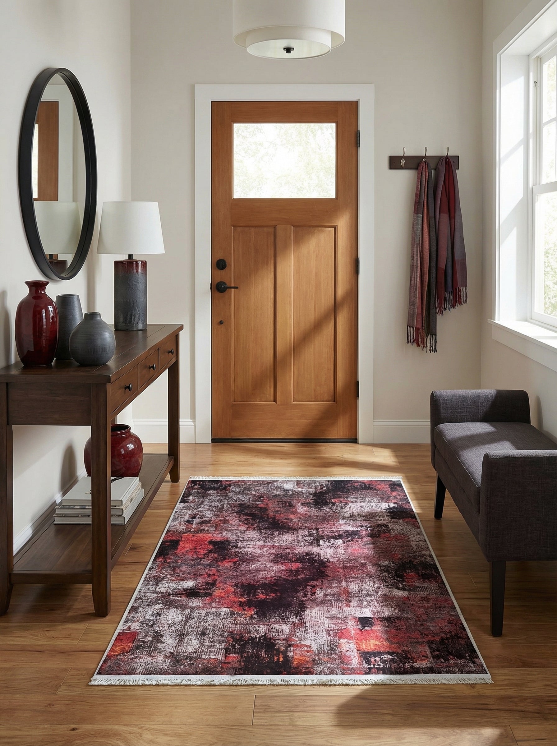 Tapis abstrait aux motifs vieillis bordeaux, noirs et gris, à franges claires, posé sur un plancher en bois d'une entrée