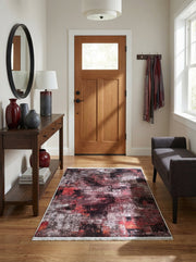 Tapis abstrait aux motifs vieillis bordeaux, noirs et gris, à franges claires, posé sur un plancher en bois d'une entrée