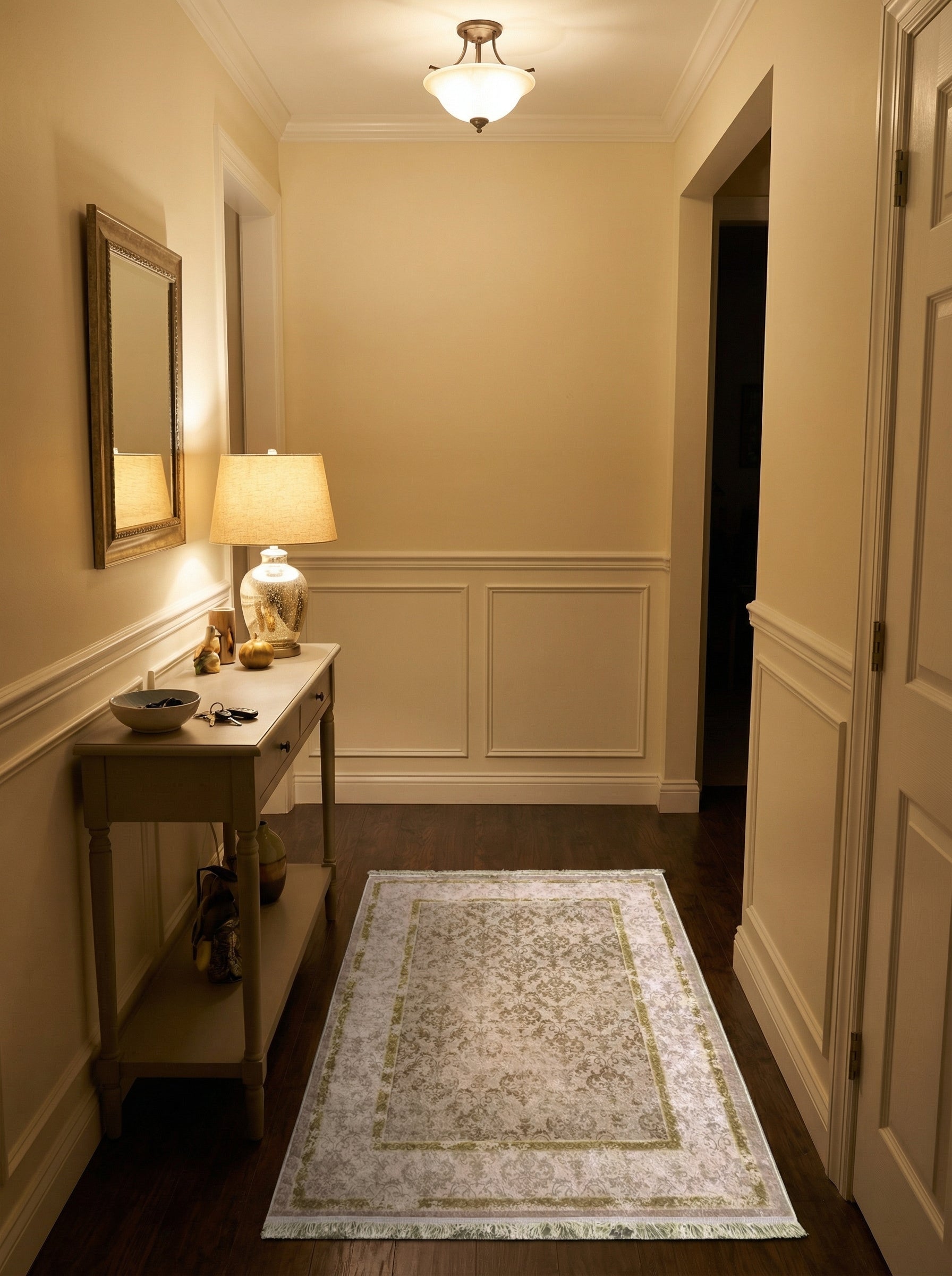 Tapis rectangulaire crème à motifs damassés beiges et verts pâles, avec des franges fines, posé sur un parquet foncé dans une entrée élégante