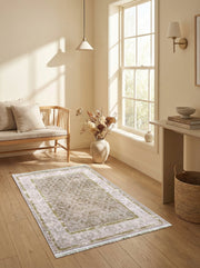 Tapis rectangulaire beige clair à motifs floraux dorés et bordures vert olive, posé sur un parquet dans un salon lumineux