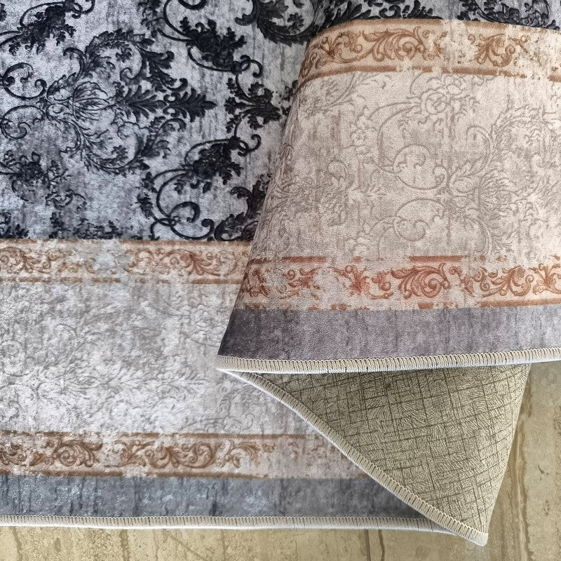 Tapis à motifs baroques gris et beige, bordures ornementales marron. Une partie du tapis est roulée, montrant le dessous texturé