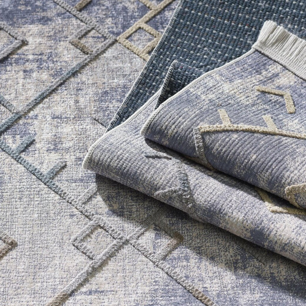 Trois tapis aux motifs géométriques et textures variées, bleu, gris et beige, avec l'un d'eux plié