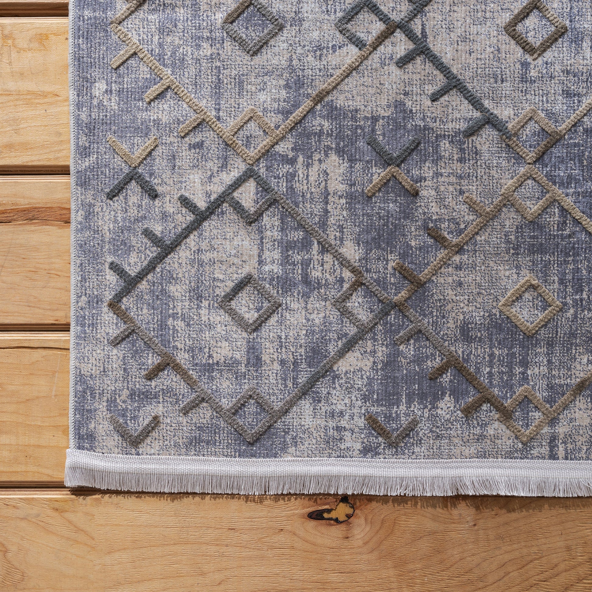 Tapis à fond moucheté gris-bleu et beige, avec motifs géométriques en relief gris foncé et marron, et frange claire