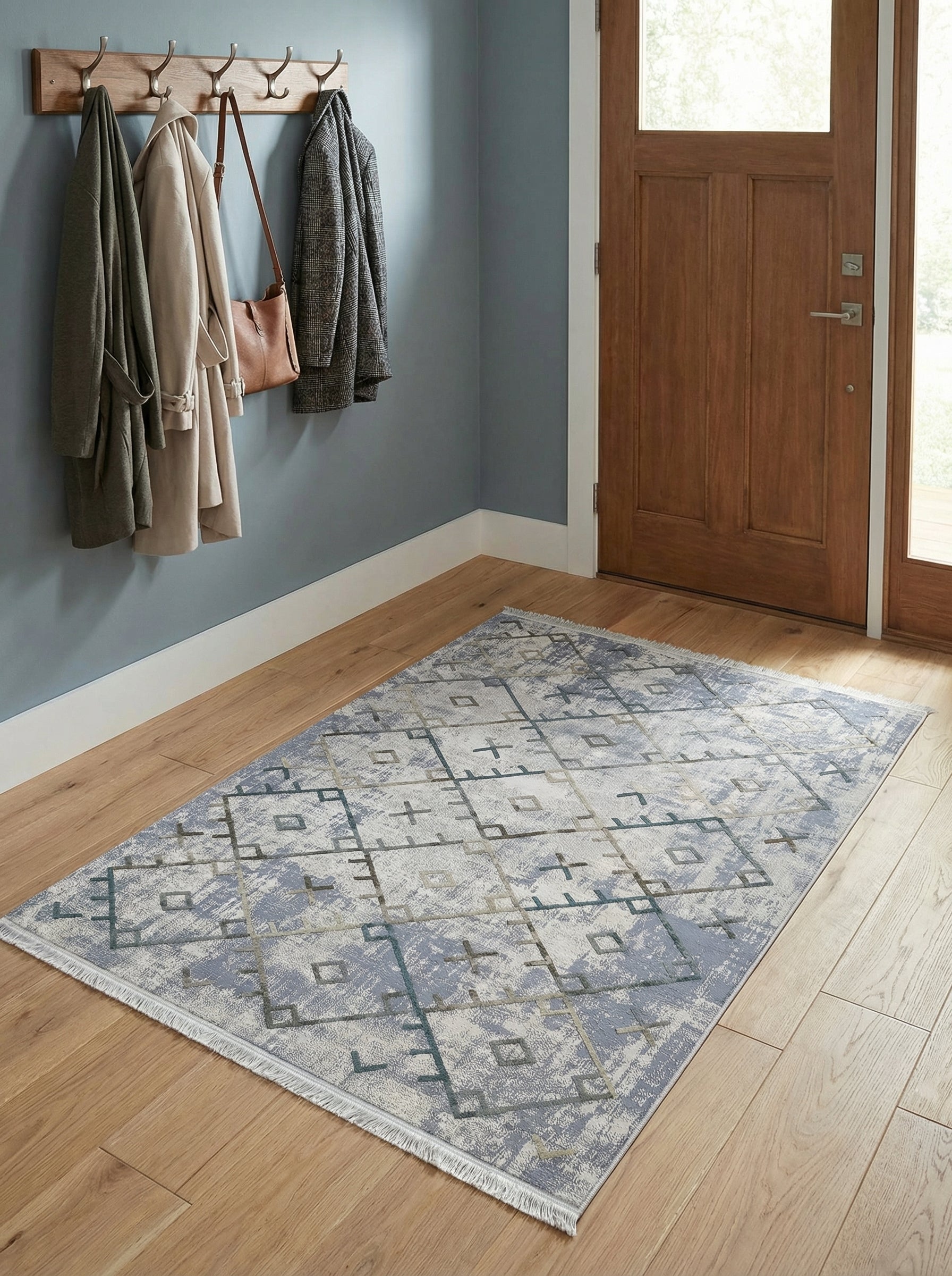 Tapis rectangulaire à franges, aux motifs géométriques abstraits bleu gris délavés et beiges, sur un parquet clair d'entrée