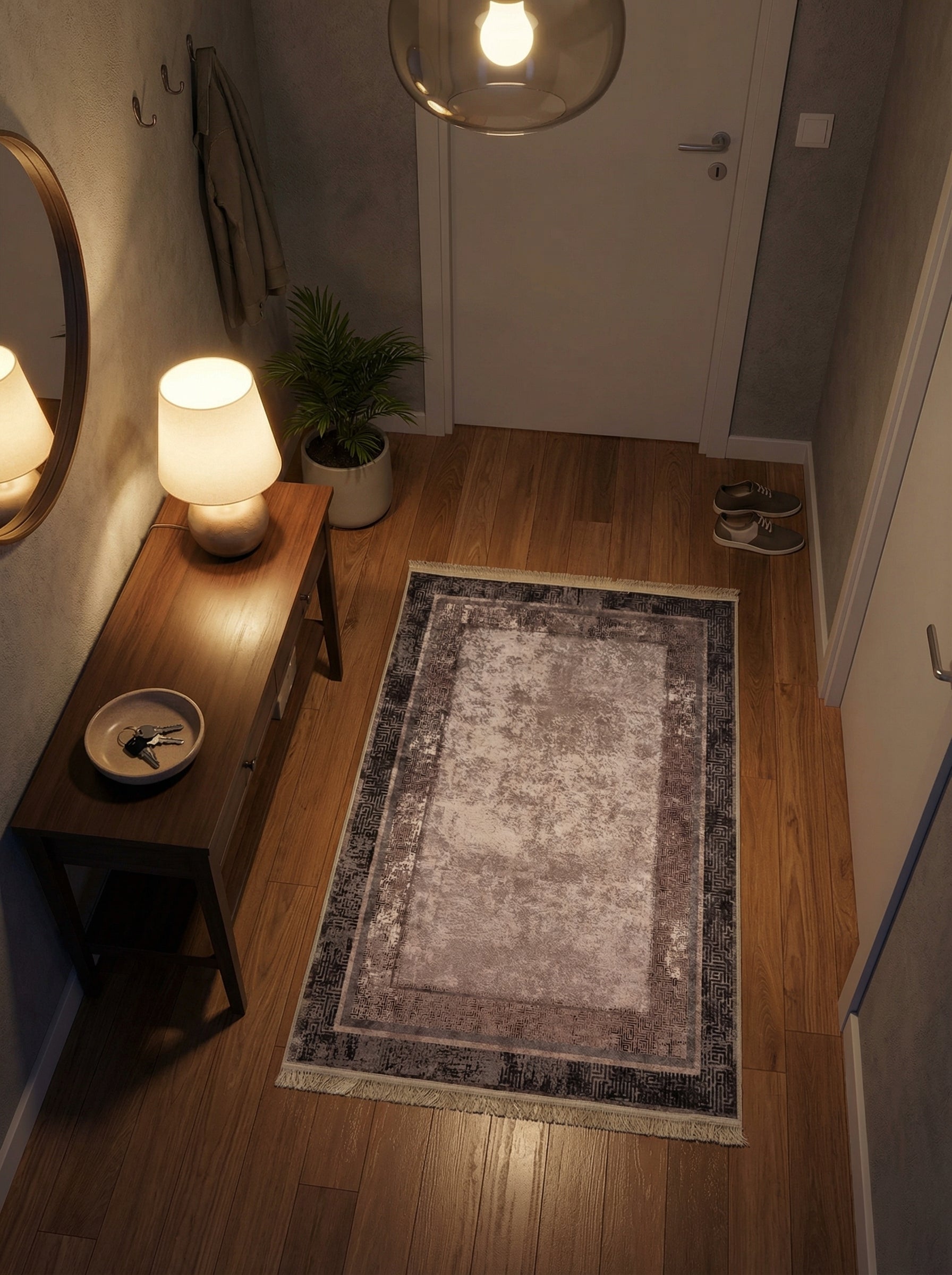 Tapis rectangulaire vieilli aux motifs géométriques complexes gris foncé et gris rosé, avec un centre crème, sur parquet dans une entrée