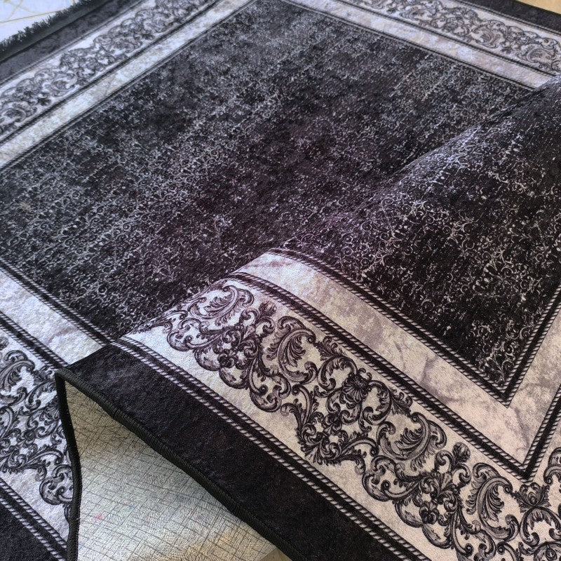 Tapis noir et gris, avec un centre au motif texturé abstrait et une large bordure à volutes ornementales