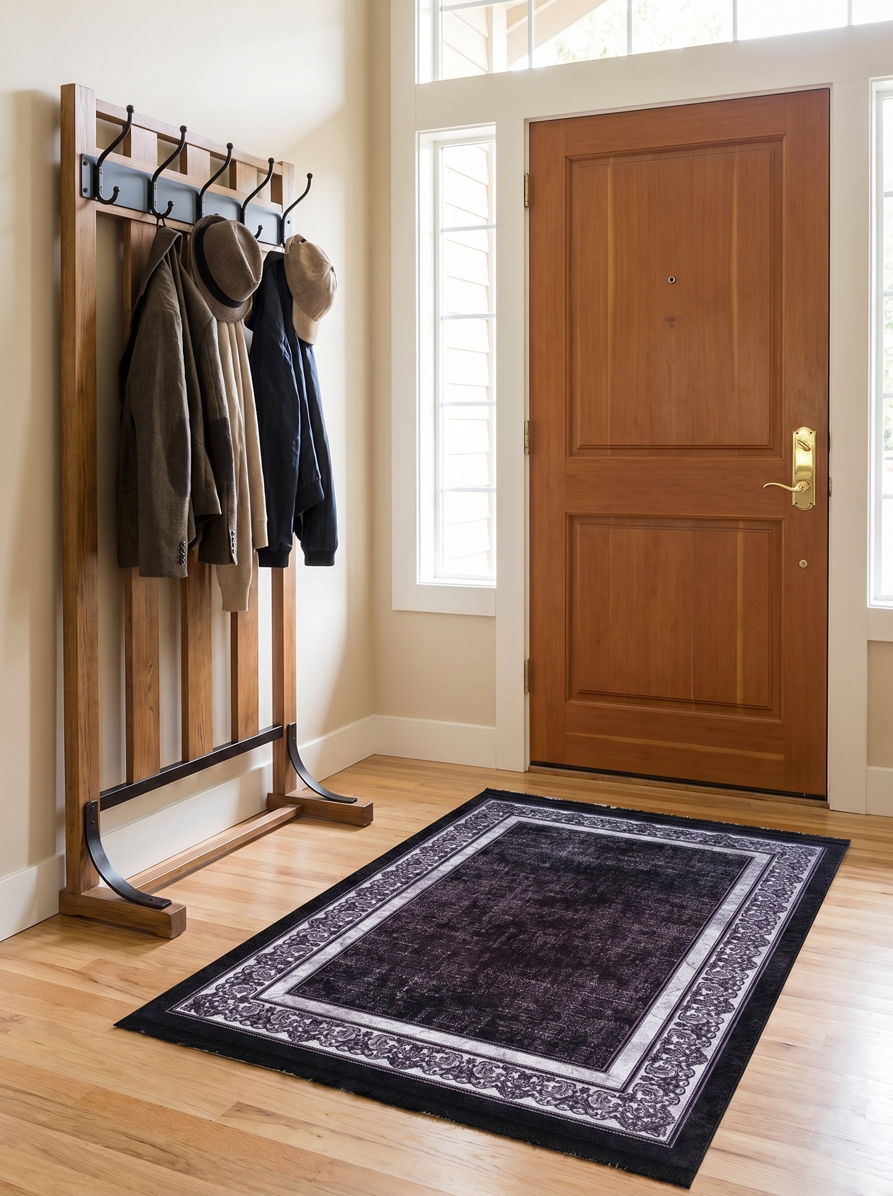 Tapis rectangulaire noir à l'aspect vieilli, bordé d'un cadre gris clair avec des motifs ornementaux, posé dans une entrée