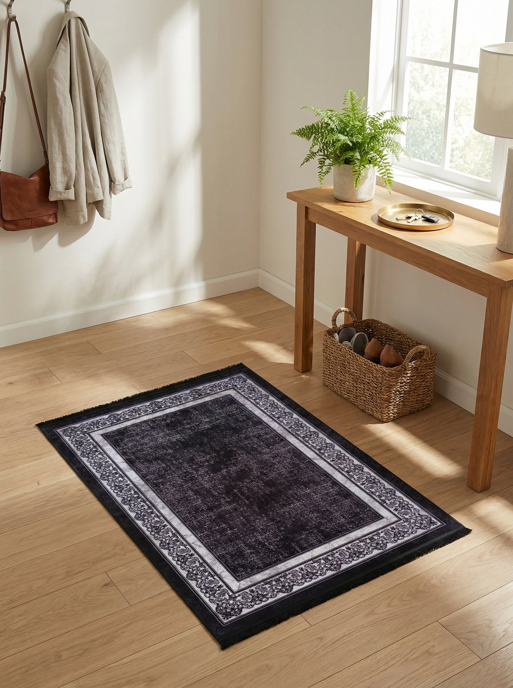 Tapis rectangulaire noir délavé, bordure gris clair à motifs floraux, sur un parquet clair dans une entrée lumineuse