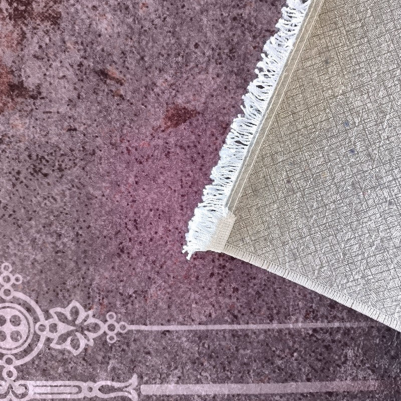 Tapis prune et bordeaux à l'aspect texturé, orné d'une bordure claire. Un coin est relevé, montrant le dessous beige à motif et les franges blanches