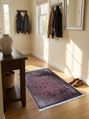 Tapis rectangulaire bordeaux vieilli à motifs ornementaux clairs sur les bordures, sur parquet dans une entrée lumineuse